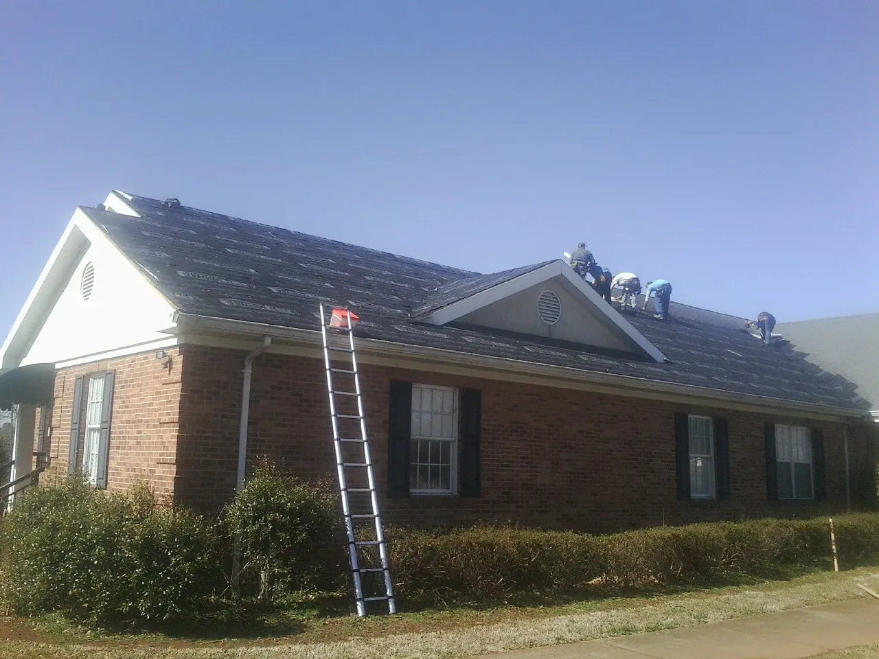 Crew tearing shingles off a brick ranch roof with a ladder set — Emergency Roof Repair work by our crew in North Highlands