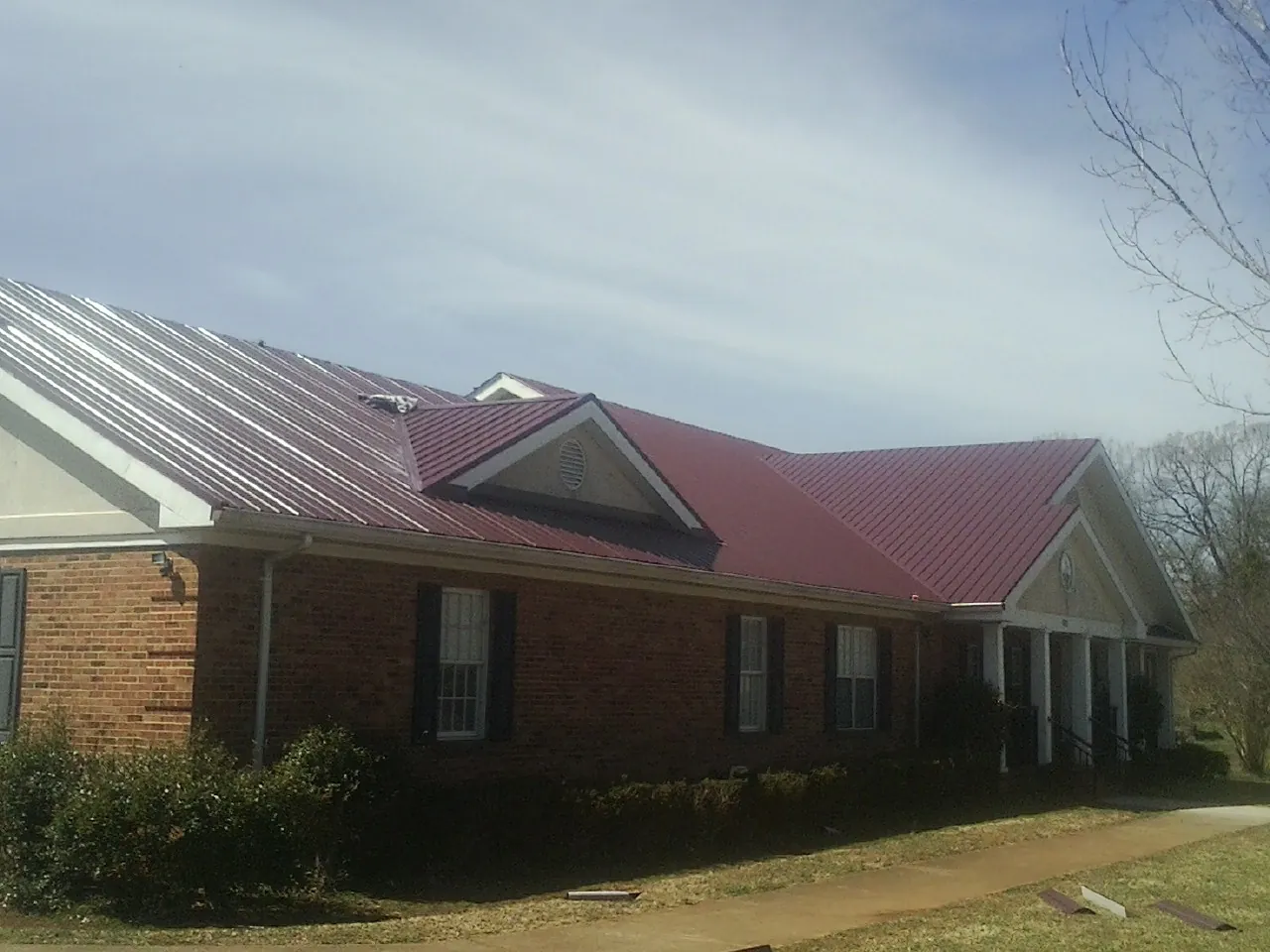 Red metal roof with gabled entries on a long brick building, from a Hail Damage Roof Repair job in North Highlands