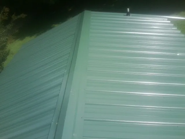 New green metal panels meeting at the ridge of a roof — Flat Roof Repair work by our crew in North Highlands